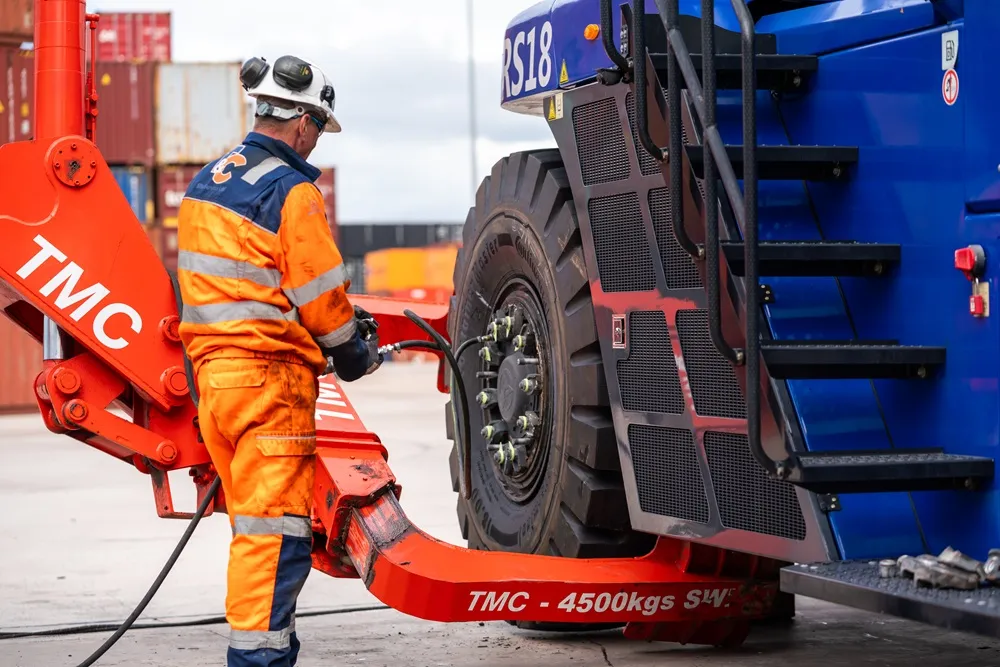 Man in an orange hi-vis outfit and hard hat, inflating a commercial tyre on construction vehicle