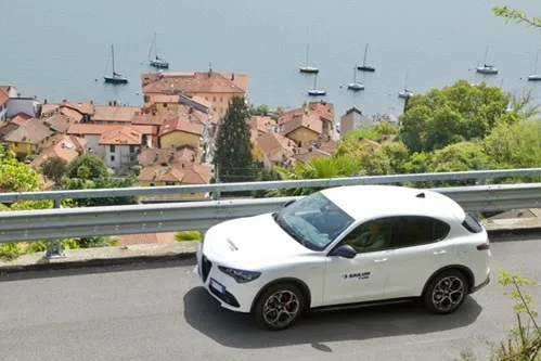 White SUV driving on a road above a village and lake somewhere in Europe