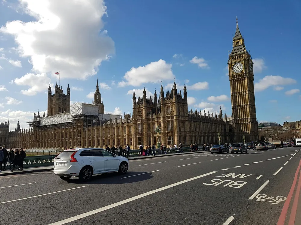 Image of the Houses of Parliament and Westminster Bridge road with a blue sky and a white car