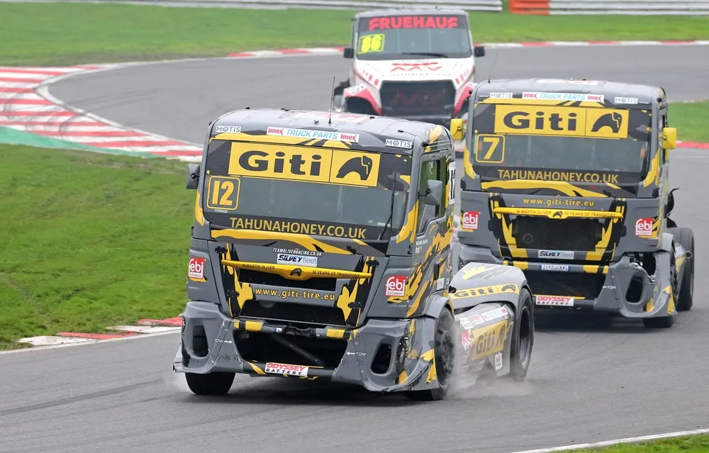 A pair of BTRC Giti Tire sponsored trucks racing around a corner Brands Hatch 2024