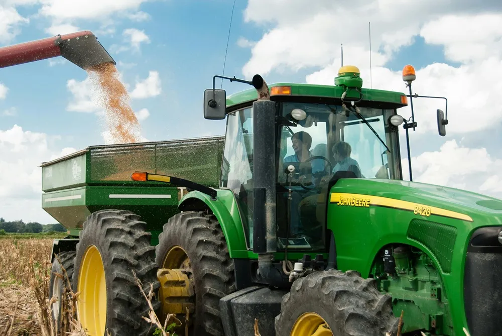 Green tractor filling up with grain into its trailer