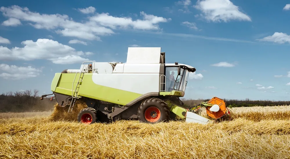 Green Combine Harvester from the side working in a field with a blue sky