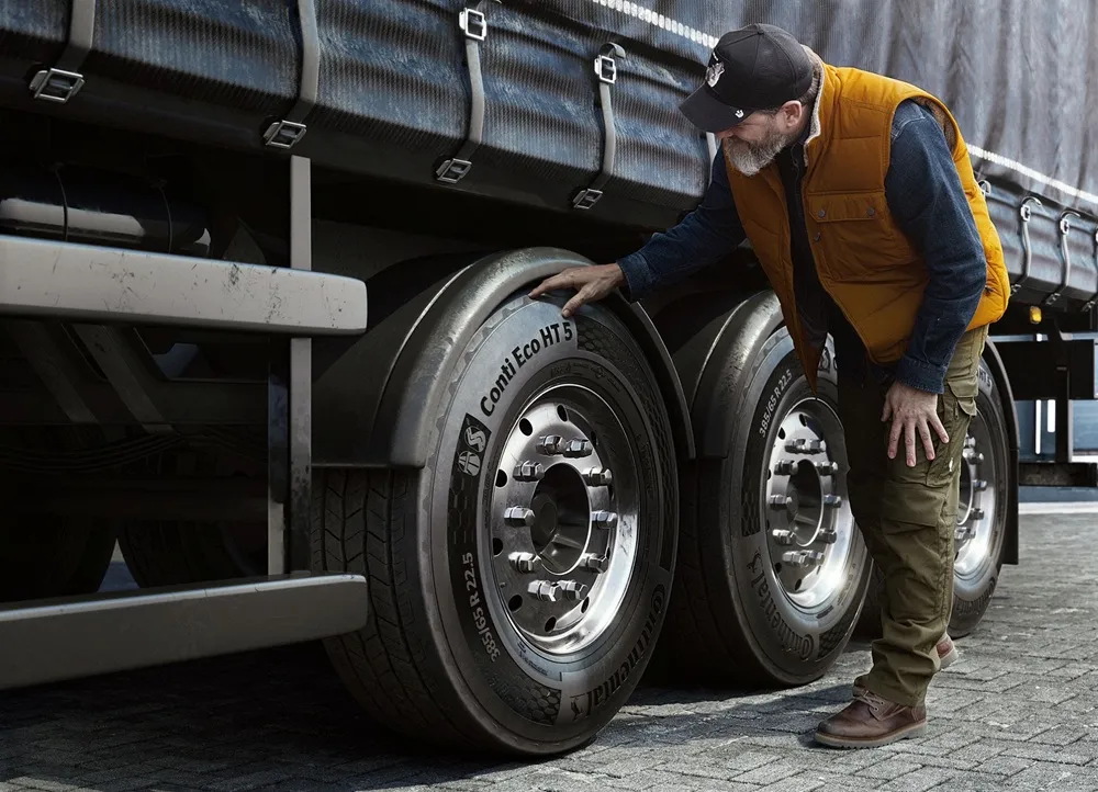 Image of a man in an orange bodywarmer and cap inspecting a truck's trailer tyre.
